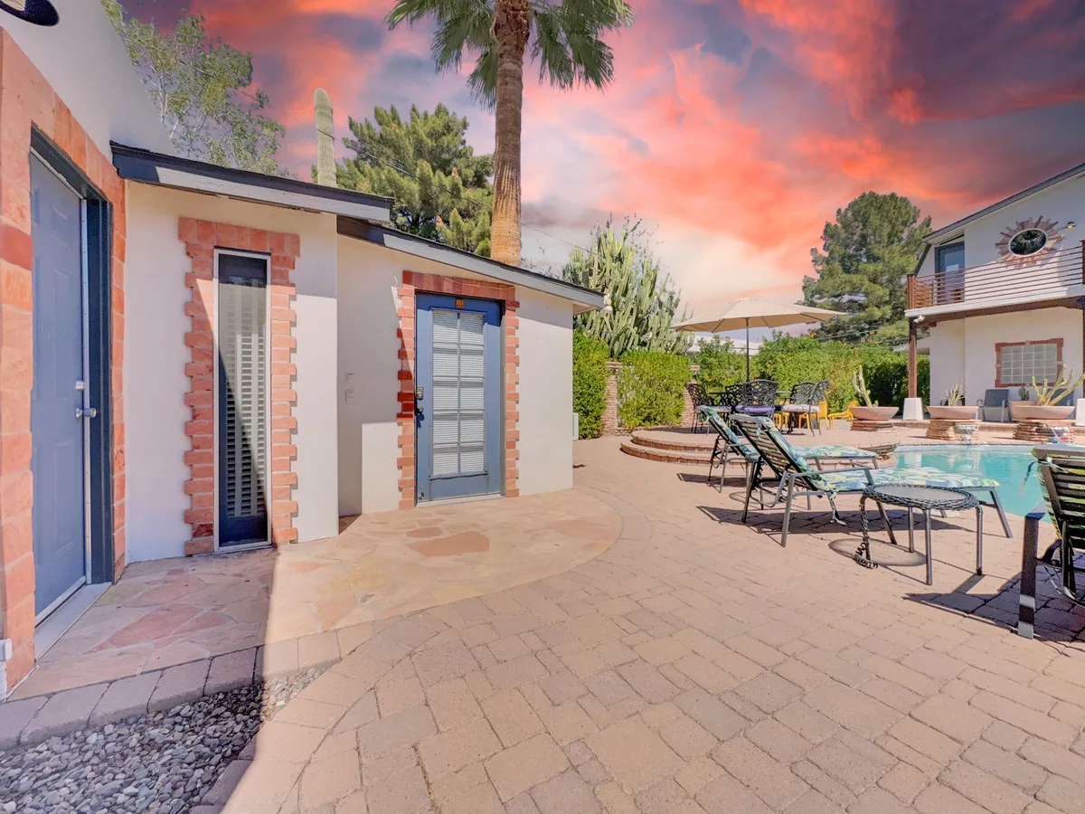 A luxurious pool area with stylish architecture, palm trees, lush greenery, and comfortable lounge chairs. The scene suggests serene afternoons spent sunbathing, swimming, or relaxing poolside as the sun sets over the tranquil landscape.