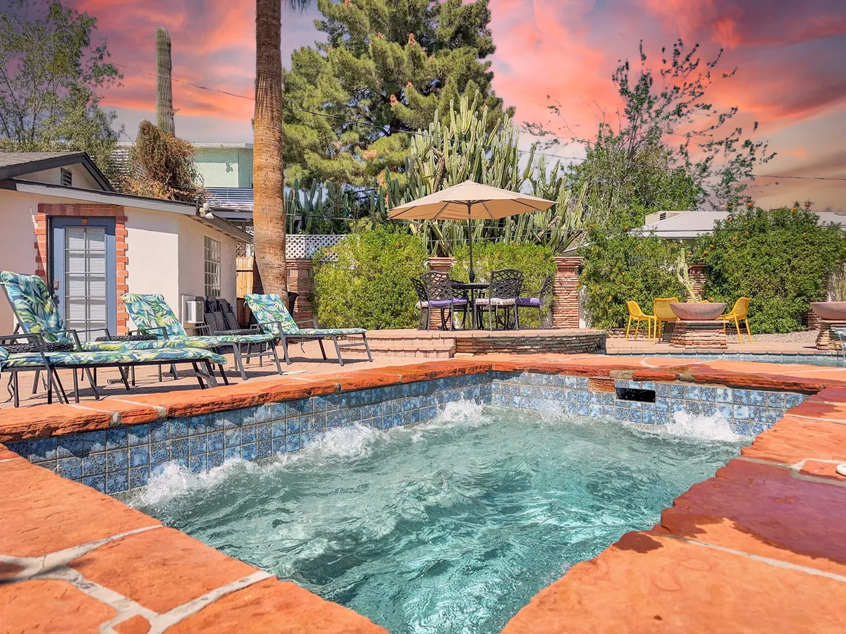 An inviting outdoor area with a hot tub, lounge chairs, an outdoor dining set, and a canopy umbrella, surrounded by lush greenery. The scene promises relaxation, al fresco meals, and memorable evenings after family outings.