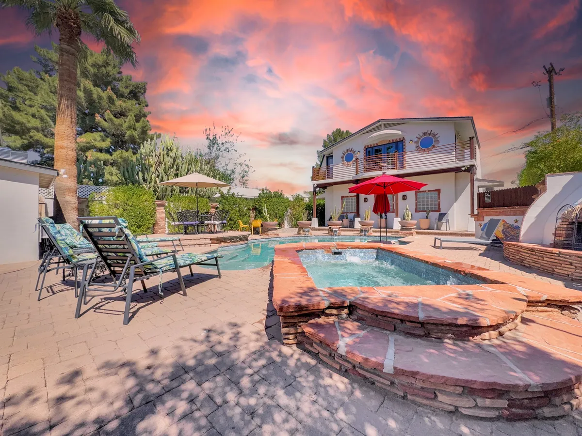 This image captures a vibrant backyard scene featuring a sparkling swimming pool, hot tub, red umbrella, palm trees, and inviting deck chairs. The space is styled for both relaxation and social gatherings, with amenities for swimming, sunbathing, barbecuing, and outdoor dining.