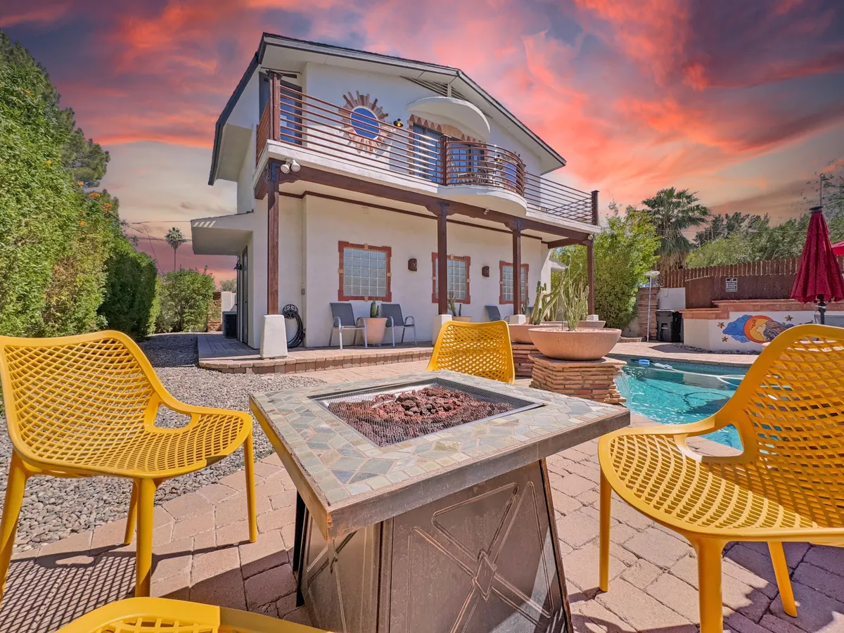 This exterior scene features yellow chairs arranged around a cozy fire pit, the swimming pool nearby, and the house's modern facade under a picturesque sunset sky. The space encourages both intimate conversations and lively group activities.