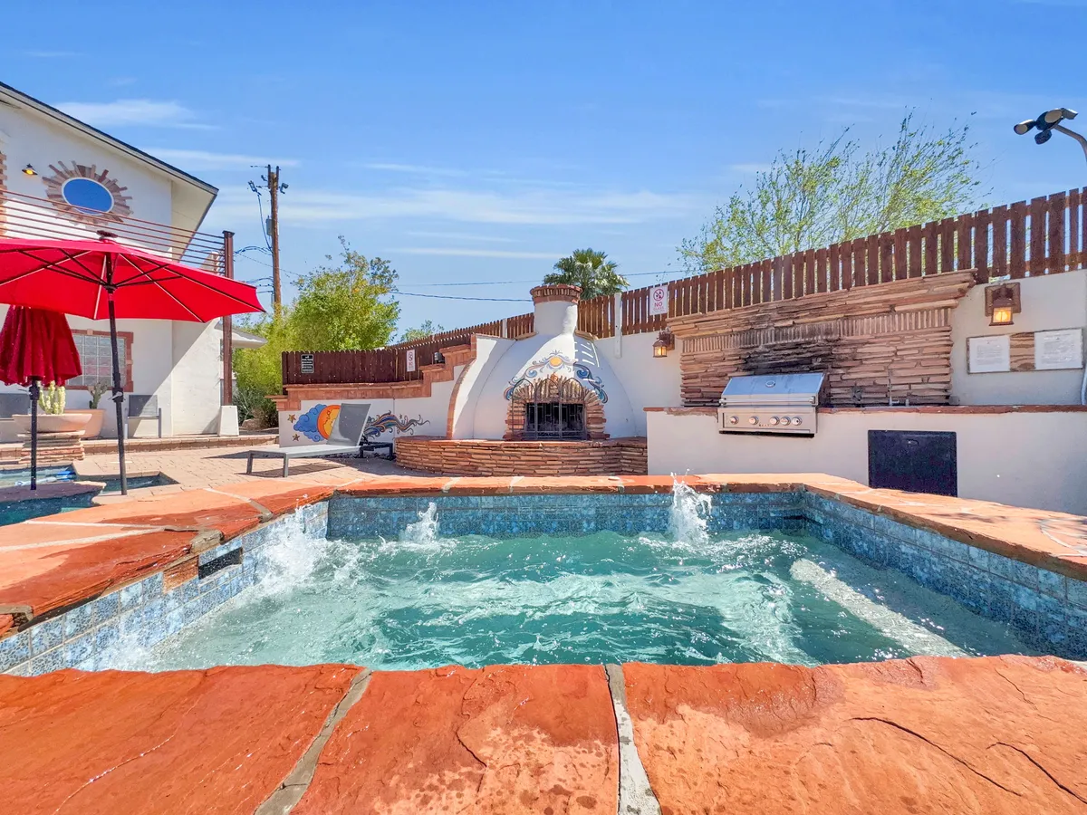An exterior shot highlighting the pool area with a fireplace, outdoor grill, and red umbrella. The relaxed environment suggests opportunities for casual barbecues and socializing after a day at the stadium or local events.