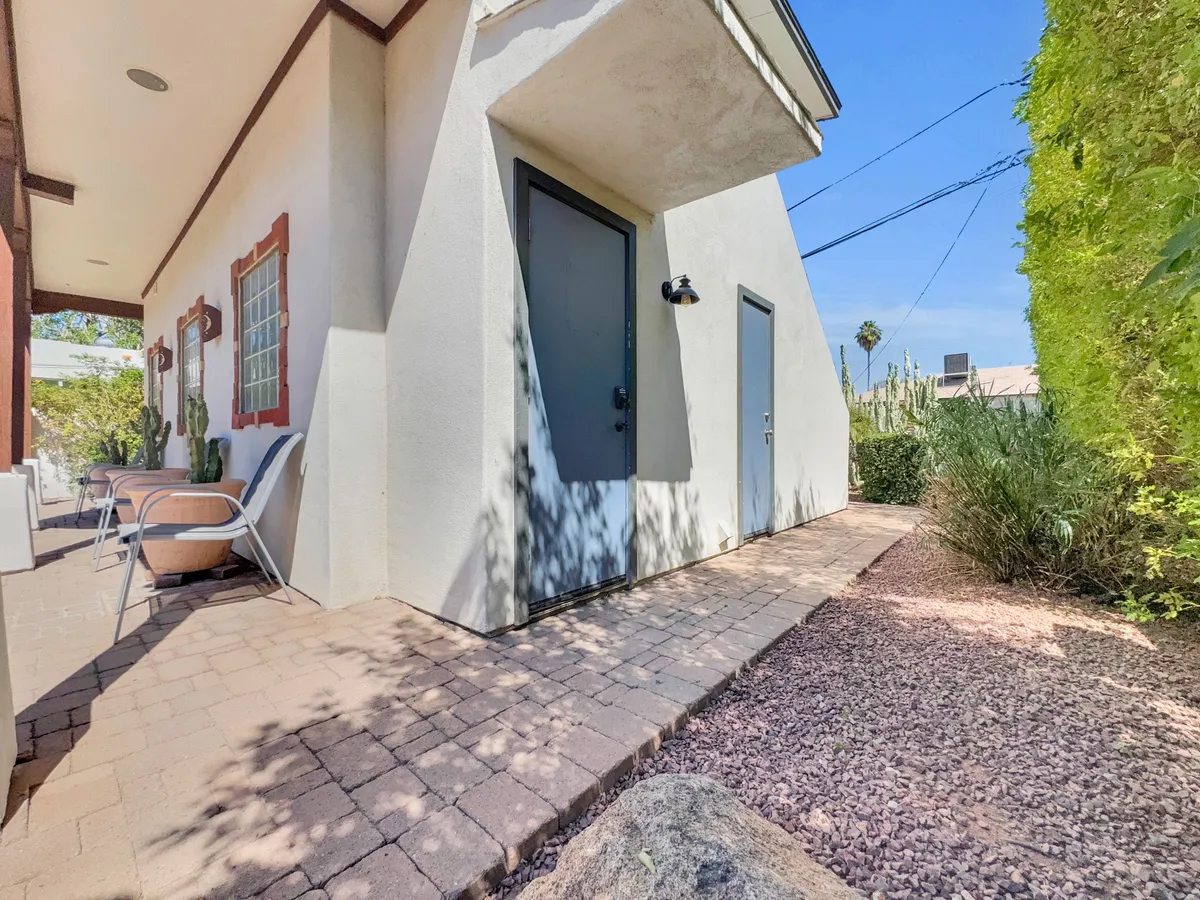 This image features an outdoor seating area framed by two doorways and attractive landscaping. The patio is inviting and suggests a welcoming spot for relaxing or enjoying time outdoors, with ample space for both people and pets to explore or lounge.