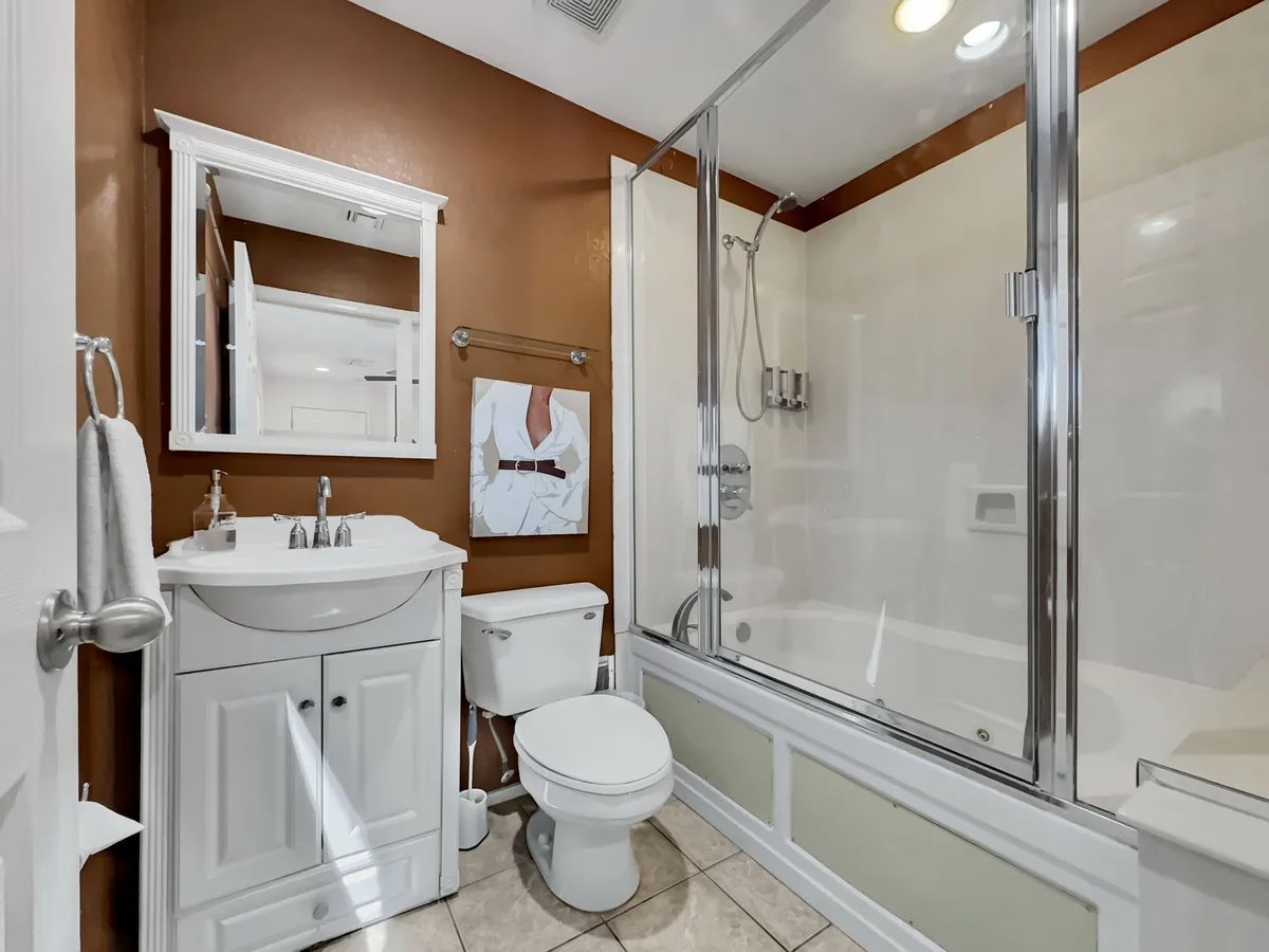 An inviting ensuite bathroom with a vanity and sink, a glass-enclosed shower, a framed mirror, and wall art. The space is practical yet stylish, suggesting a luxurious and rejuvenating bathing experience after a long day.