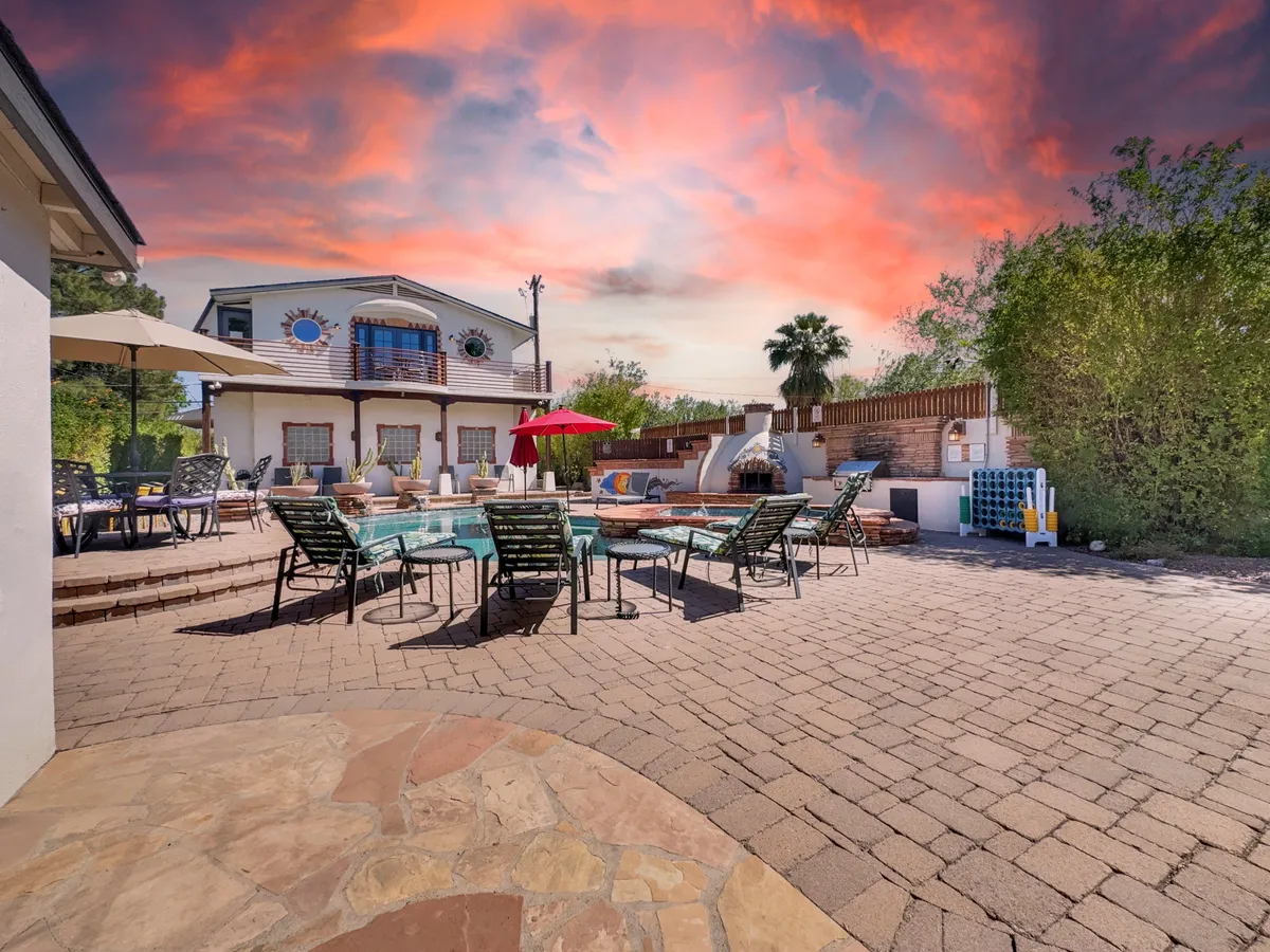 A cheerful backyard scene featuring a sparkling swimming pool, patio seating, colorful umbrellas, and well-maintained landscaping. The setup hints at both lively social gatherings and relaxed afternoons under the sun or shade.