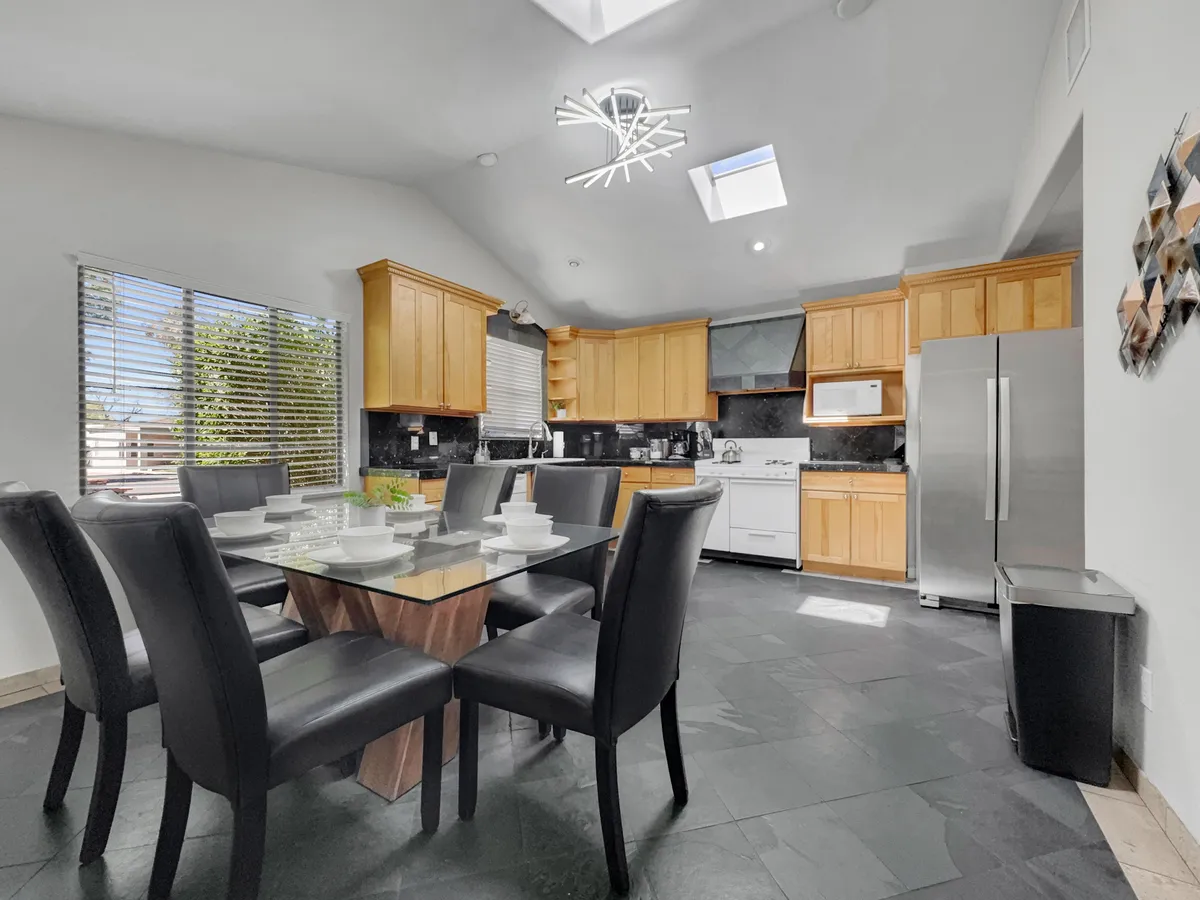 A view of the dining area seamlessly connected to the kitchen, with a spacious dining table, kitchen cabinets, and appliances visible. The skylight above enhances the inviting and functional mood, perfect for family meals and gatherings.