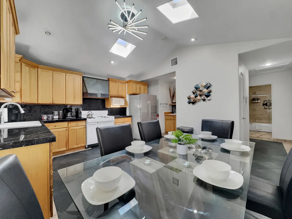 A stylish dining area adjacent to the kitchen, featuring a modern light fixture, skylights, and comfortable seating at a large dining table. The cabinetry and overall layout highlight the space’s suitability for cooking and entertaining guests.